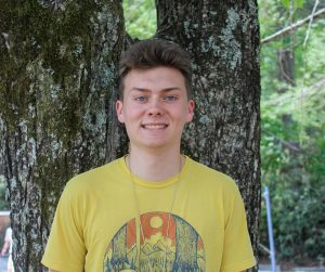 boy in yellow shirt standing in front of tree